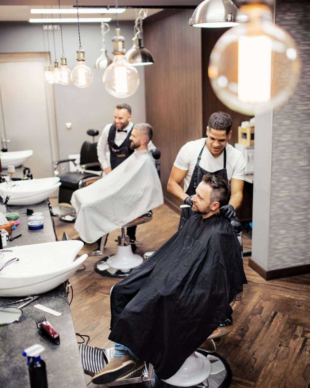 A high angle view of man clients visiting haidresser and hairstylist in barber shop.